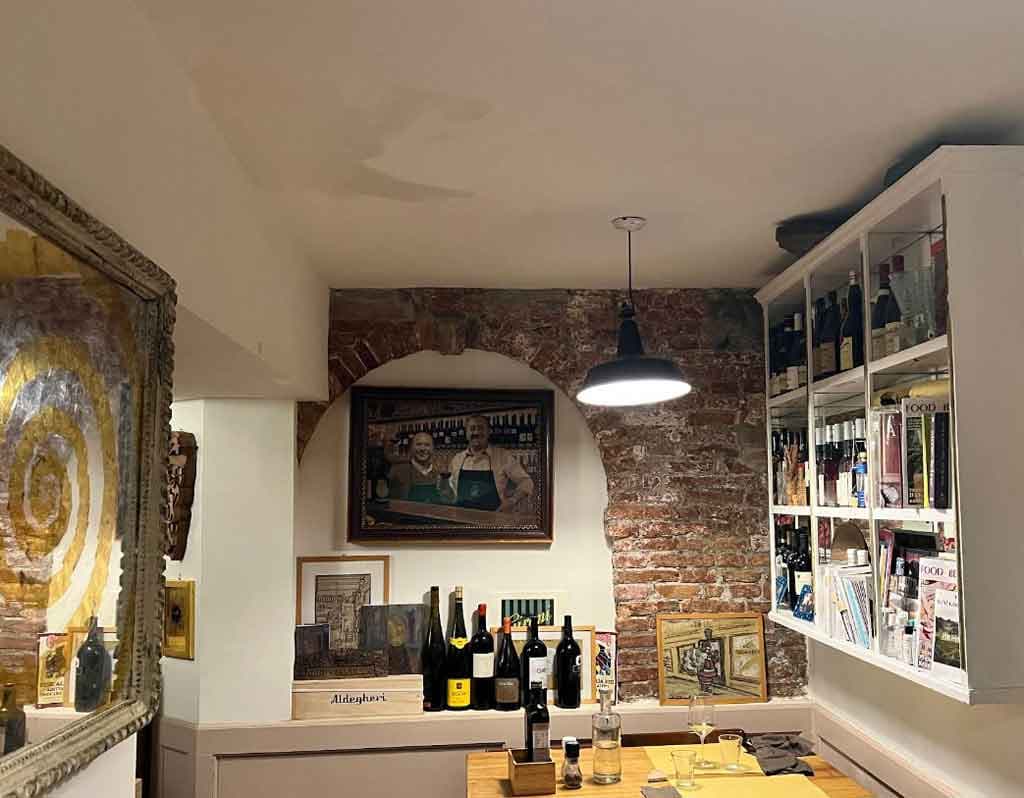 Intérieur du bar à vin Enoteca Mascareta à Venise, avec ses bouteilles et ses sièges adossés à un mur de briques rustique